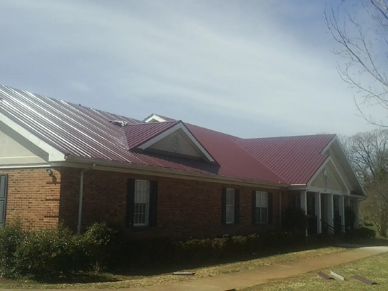 Red metal roof with gabled entries on a long brick building, from a Hail Damage Roof Repair job in Danville